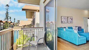 Een balkon met een stoel, een blauwe bank en een grote schuifdeur die leidt naar een kamer met twee ingelijste foto's.
