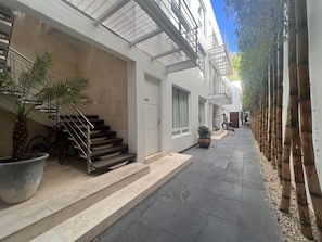 A narrow street with a building featuring a staircase, a bicycle, and potted plants.