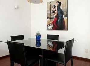 Zona pranzo con tavolo in vetro, sedie nere e vaso blu.