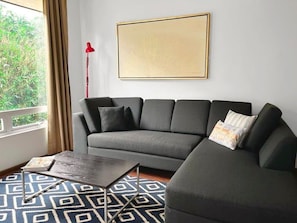 A modern living room with a grey sofa, a patterned rug, a framed artwork on the wall, and a red floor lamp.