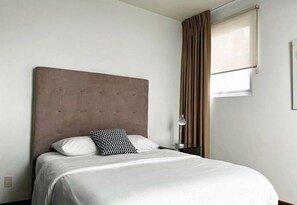A hotel room with a bed, a nightstand, a lamp, and a window with curtains.