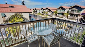 Ein Balkon mit Glastisch und Stühlen, mit Blick auf einen Fluss und eine Reihung von Gebäuden mit roten Dächern.