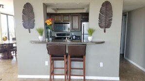 A kitchen with a central island, bar stools, and decorative leaf wall art. - Our House at the Beach E-603 Phenomenal Views and Location (Siesta Key)