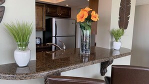 A kitchen with granite countertops, a stainless steel refrigerator, and wooden cabinets. There are two potted plants on the counter. - Our House at the Beach E-603 Phenomenal Views and Location (Siesta Key)