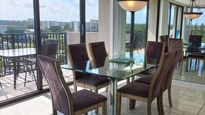 A modern dining area with glass tables and chairs, large windows offering city views, and a balcony with outdoor seating.