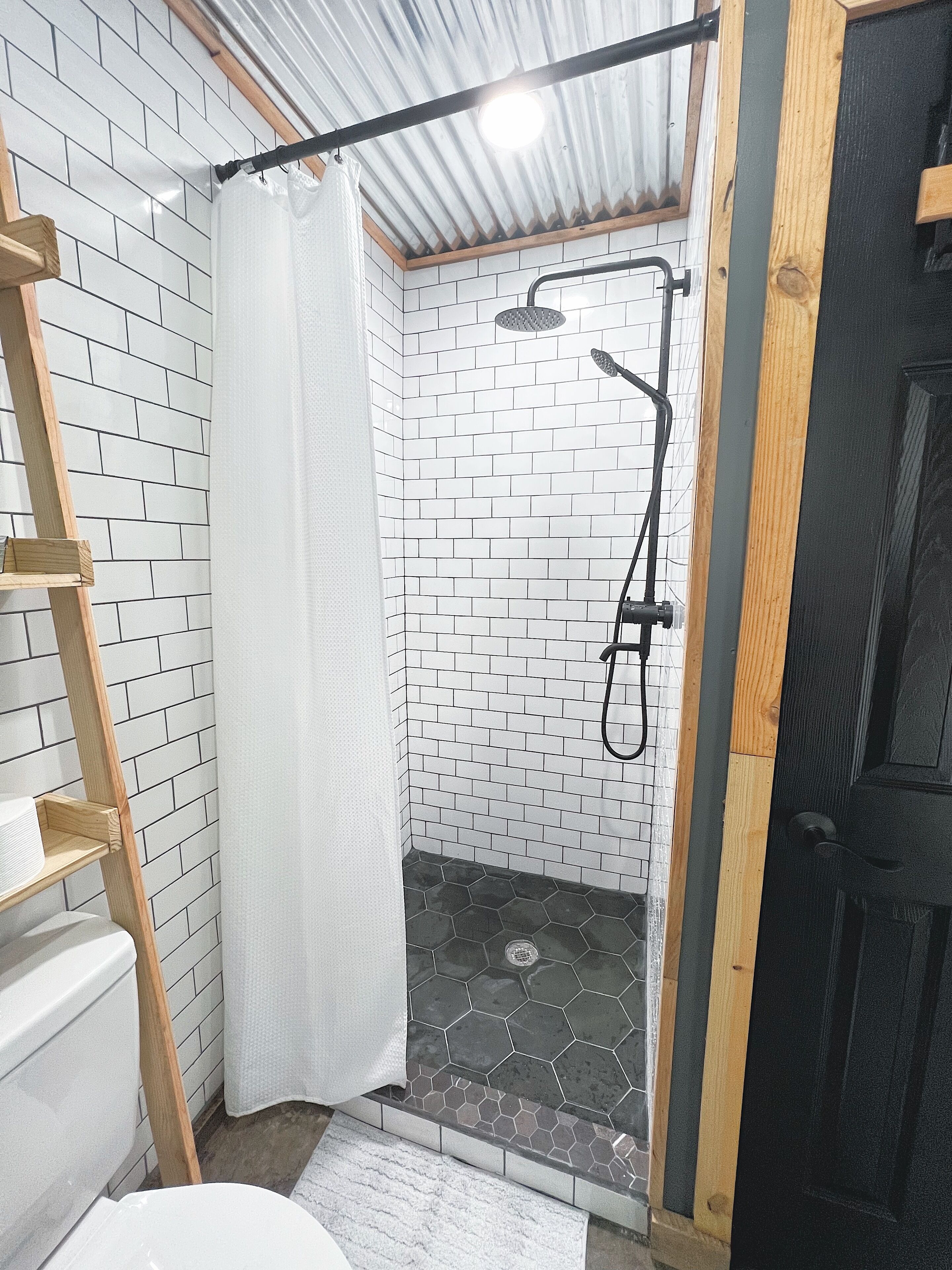 Zona de ducha con ducha, escalera de madera y cortina blanca.