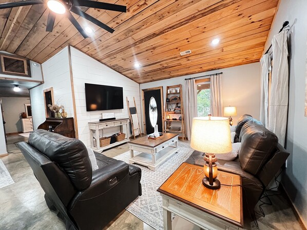 A living room with wooden ceiling, a flat-screen TV, leather sofas, a coffee table, and a lamp.