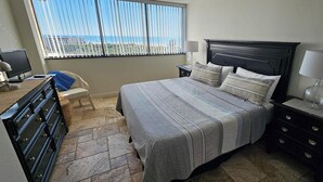 Een slaapkamer met een bed, een dressoir, een nachtkastje, een stoel en een raam met jaloezieën.