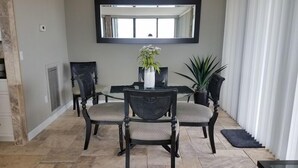 A dining area with a round table, four chairs, a vase with flowers, and a potted plant. - Our House at the Beach E-704 Best view of the Gulf! (Siesta Key)