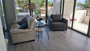 Een moderne woonkamer met een bank, fauteuil, glazen salontafel en uitzicht op het buiten.