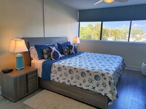 Ein Schlafzimmer mit Bett, Nachttischen, einer Lampe und einem Fenster mit Blick auf Bäume.