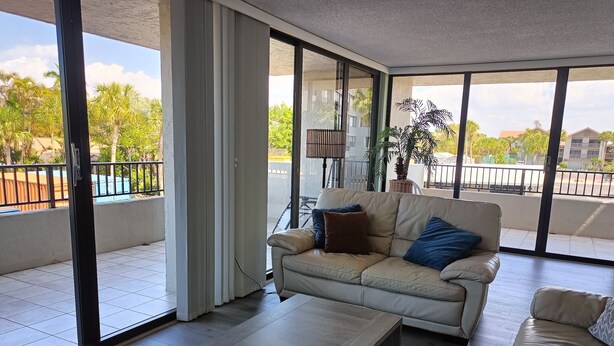 A modern living room with a beige sofa, a wooden coffee table, and a large sliding glass door leading to a balcony. - Next to the Beach - Our House at the Beach W-103 (Siesta Key)