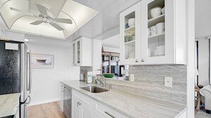 Eine moderne Küche mit weißen Schränken, einer Marmorarbeitsplatte und einem Deckenventilator.