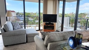 Uma sala de estar moderna com um sofá cinzento, uma mesa de centro de vidro e uma televisão de tela plana sobre um suporte de madeira.
