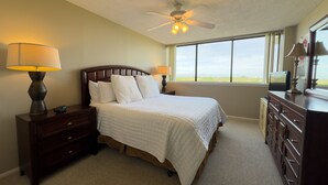 Une chambre à coucher avec un grand lit, deux tables de chevet avec des lampes, une commode et un ventilateur de plafond.