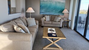 Un salon avec un canapé, une table basse et un tableau représentant une vague.