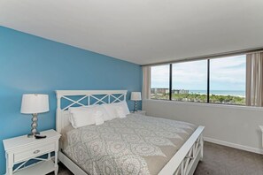 A bedroom with a large bed, two bedside tables, and a window with a view of the ocean. - Our House at the Beach W-601 Luxury Quality Unit with Ocean View (Siesta Key)