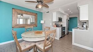 A modern kitchen with white cabinets, a microwave, and a stove. There is a dining area with a round table and chairs.