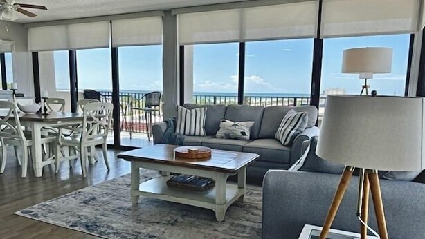 A spacious living room with a balcony, a dining area, and a large window offering a view of the ocean. - Our House at the Beach W-602 Beautiful Beach View! (Siesta Key)