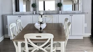 A dining area with a wooden table and white chairs, a ceiling fan, and a window with curtains. - Our House at the Beach W-602 Beautiful Beach View! (Siesta Key)