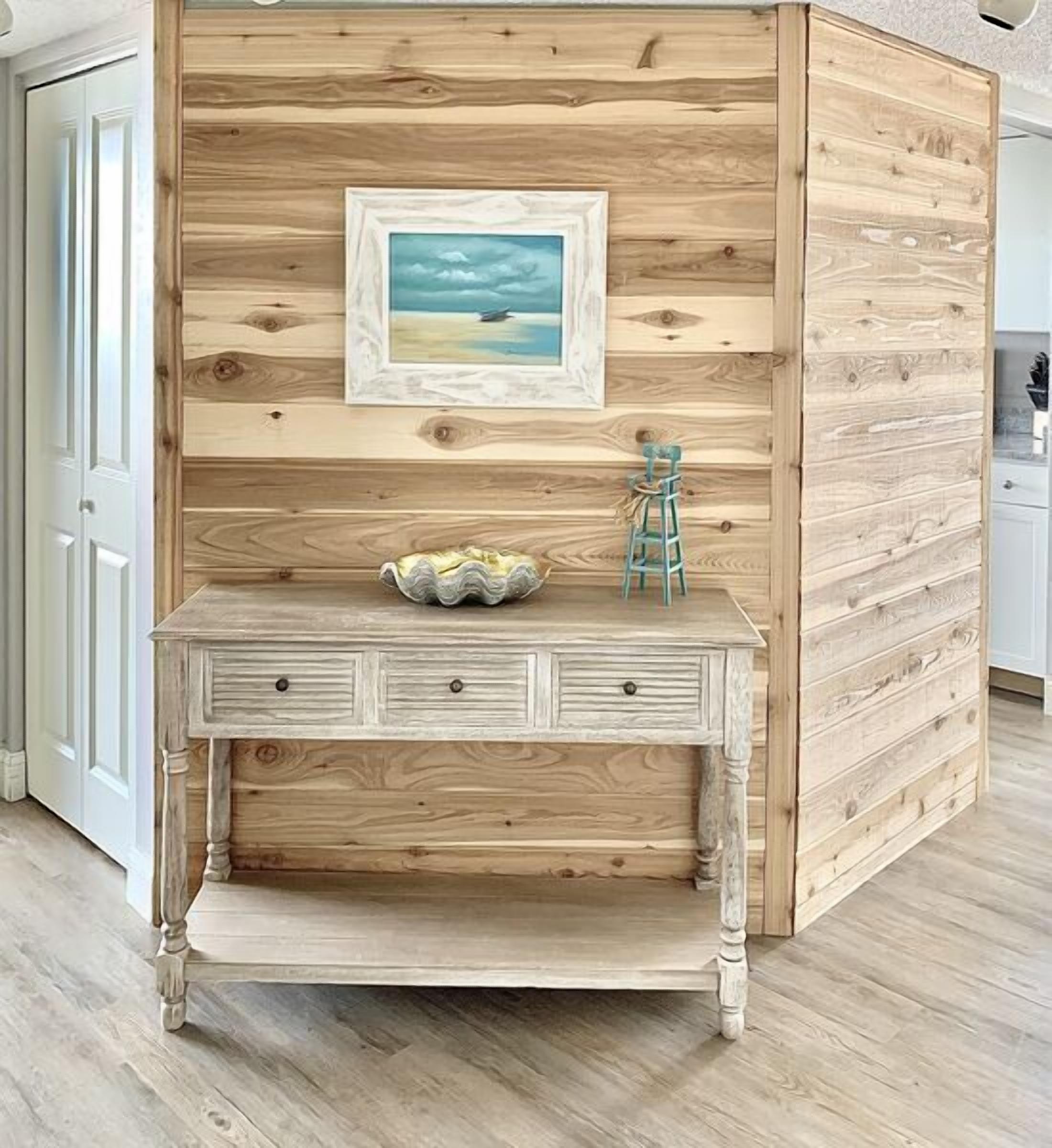 A rustic wooden desk with drawers and a shelf, a framed picture on the wall, and a small blue stool.
