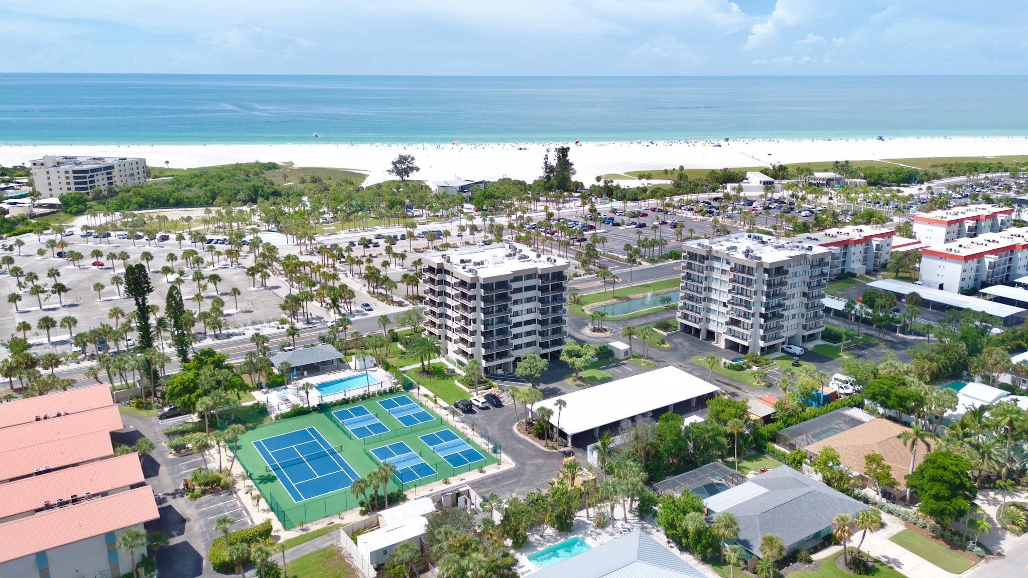 A resort with multiple buildings, a beach, and a tennis court.