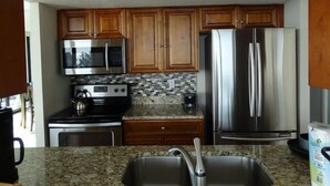 A kitchen with wooden cabinets, stainless steel appliances, a granite countertop, and a stainless steel sink. - Our House at the Beach W-701 Best Panoramic Views! (Siesta Key)