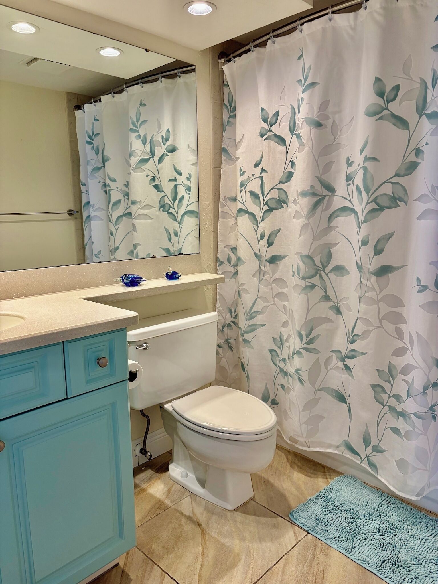 A bathroom with a toilet, sink, mirror, and shower curtain with a leaf pattern.