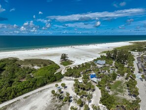An aerial view of a beach resort with a large sandy beach, a parking area, and a building with a blue roof. - Our House at the Beach W-702 Beach View Beauty, Updated! (Siesta Key)