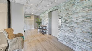 Passadís de disseny modern, amb un mur amb dibuixos, una cadira de vimet, una taula petita i una planta en test.