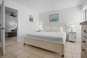 A bedroom with a bed, bedside tables, a dresser, a ceiling fan, and two paintings on the wall. - Ground-floor Condo with Community Pool and Beach Access - Sea Club II Unit 2B (Siesta Key)