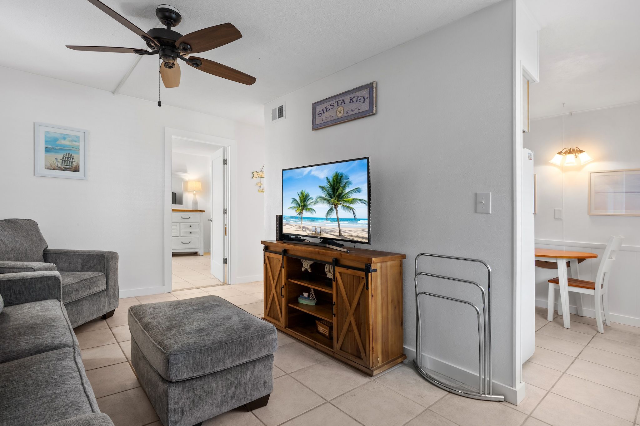 A living room with a television, grey sofa, ottoman, wooden cabinet, and a ceiling fan.