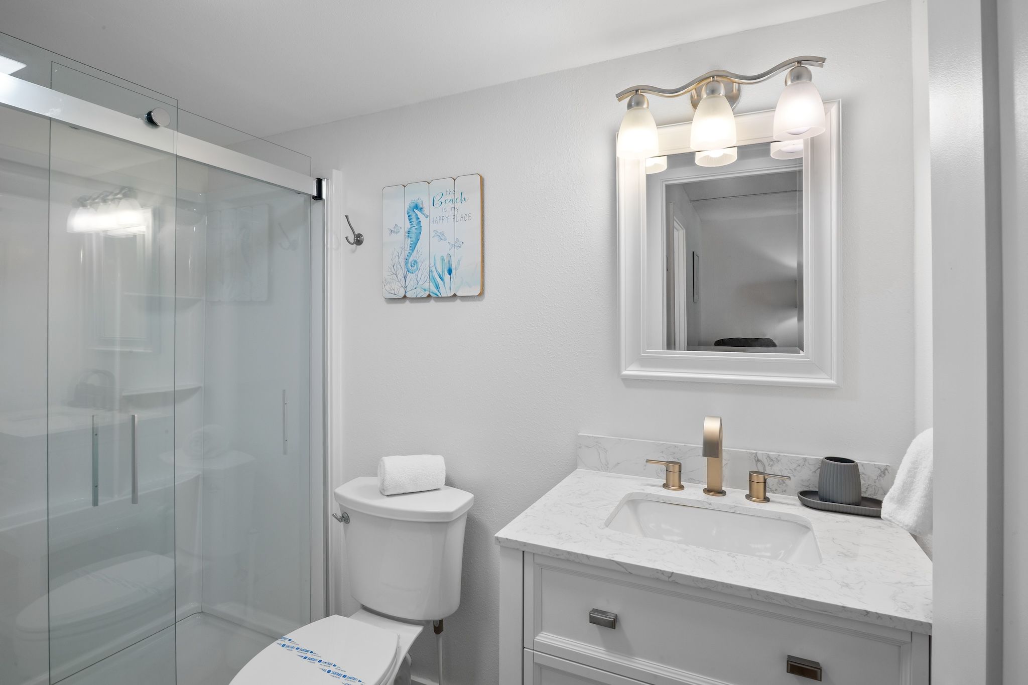 Een moderne badkamer met een douchecabine van glas, een toilet, een wastafel met een marmeren blad en een badkamermeubel met een spiegel.