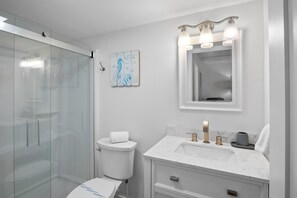 A modern bathroom with a glass shower enclosure, a toilet, a sink with a marble countertop, and a vanity with a mirror. - Ground-floor Condo with Community Pool and Beach Access - Sea Club II Unit 2B (Siesta Key)