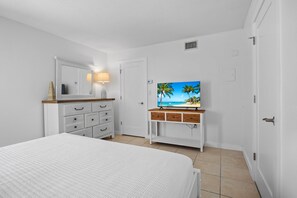 A bedroom with a bed, a dresser with drawers, a television on a stand, and a door.