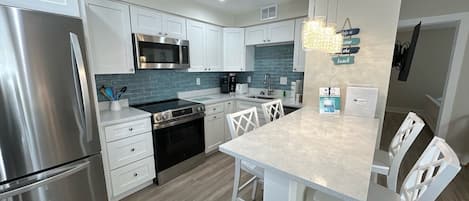 A modern kitchen with stainless steel appliances, white cabinetry, a granite countertop, and a hanging light fixture.