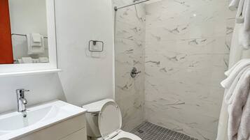 Un baño moderno con lavamanos, inodoro y zona de ducha blancos.