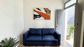 A living room with a patterned floor, a dark blue sofa, a wall-mounted abstract painting, and a potted plant.