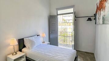 A bedroom with a bed, bedside lamps, a ceiling light, a door leading to a balcony, and a wall-mounted air conditioner.