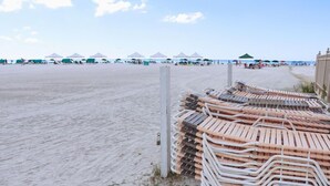 A beach with rows of sun loungers stacked against a white post, and beach umbrellas in the background. - Townhouse with Beach Access, Shared Pool - Siesta Beach House 308 (Siesta Key)