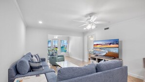 A modern living room with a grey sofa set, a flat-screen TV, and a ceiling fan. - Sunset Royale - 106- Directly Across from Siesta Key Beach! (Siesta Key)