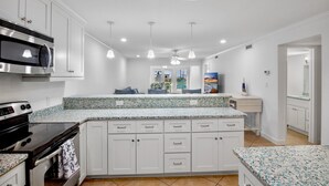 A modern kitchen with white cabinetry, a built-in microwave, and a granite countertop. - Sunset Royale - 106- Directly Across from Siesta Key Beach! (Siesta Key)