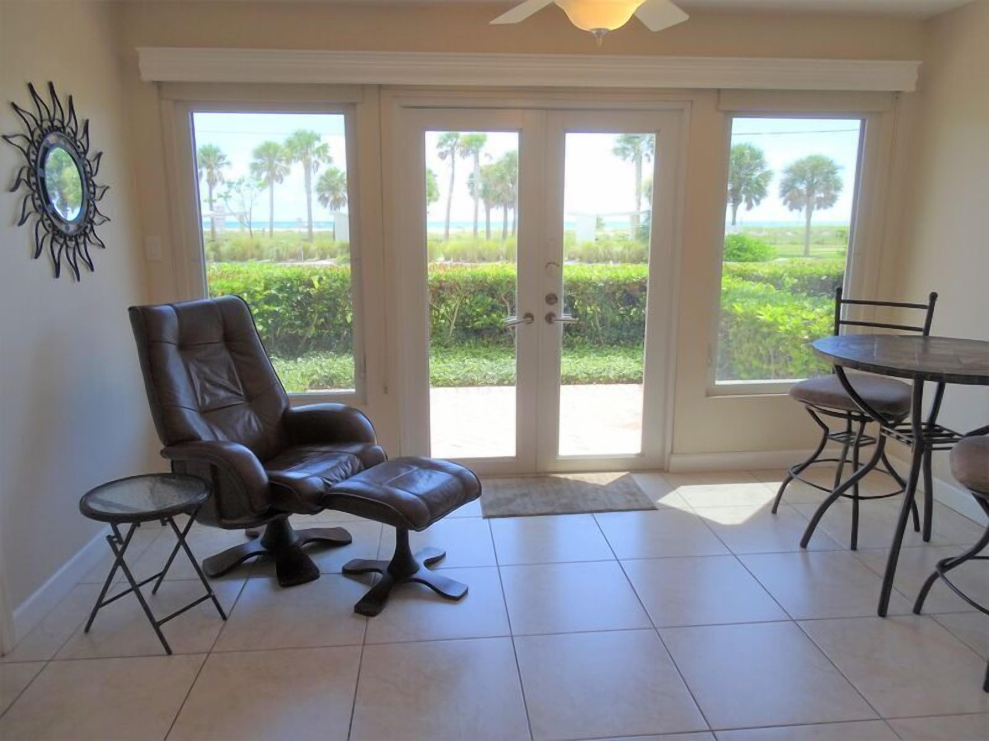 A room with a leather chair, a small table, and a view of a landscaped area through glass doors.