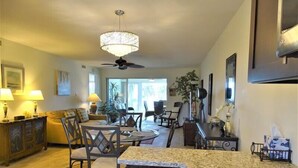 A spacious living area with a dining table, chairs, a ceiling fan, and a large window providing natural light. - Sunset Royale - 200- Beautiful two bedroom, two bathroom condo with great views. (Siesta Key)