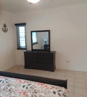 A bedroom with a bed, dresser, mirror, and a window with blinds.