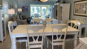 Un espace repas avec une table et des chaises blanches, un lustre et une vue sur l’extérieur.