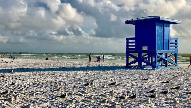 A beach with a blue lifeguard tower, sandy beach, and a cloudy sky. - Sunset Royale - 302- Stunning Sunset Views (Siesta Key)