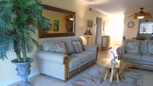 A living room with a sofa, a coffee table, a potted plant, and a mirror on the wall. - Sunset Royale - 302- Stunning Sunset Views (Siesta Key)