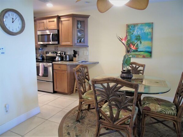 A kitchen with wooden cabinets, a microwave, and a stove. There is a dining table with chairs and a painting on the wall. - Sunset Royale - 302- Stunning Sunset Views (Siesta Key)