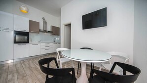 A modern kitchen with white cabinets, a built-in oven, and a stainless steel range hood. There is a round glass table with four chairs, and a flat-screen TV mounted on the wall. - Holiday Home Relax - One Bedroom Holiday Home with Hot Tub (Podstrana)
